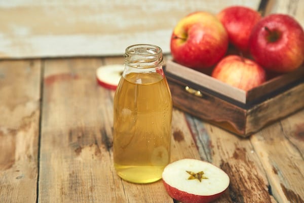 Apple cider vinegar. Glass Bottle of apple organic vinegar on wooden table. Healthy organic drink food. Bottle of fresh cider near autumn red apples. Rustic background,  Space for text