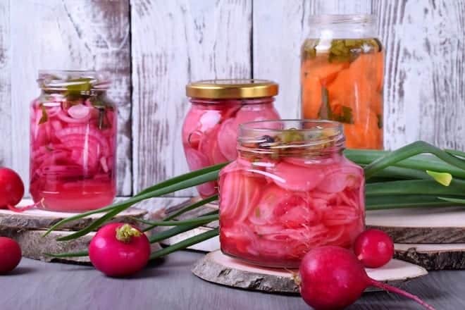 glass jars filled with pickled pink radishes on wood, with spring onions and whole radishes