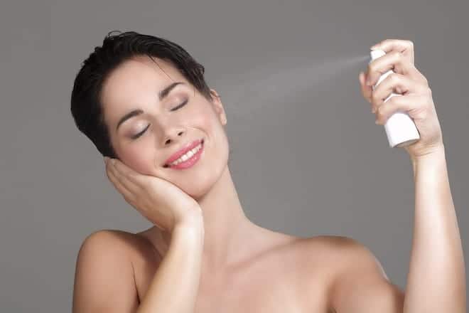 Beautiful woman applying spray water on face on neutral background