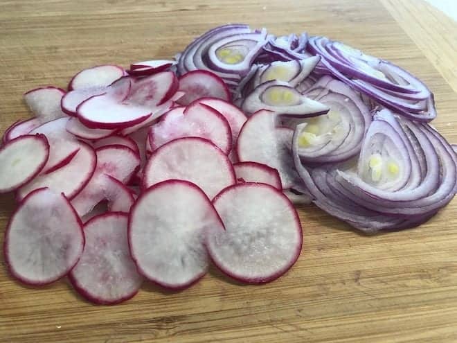 thinly sliced radish and pink onion on wooden board