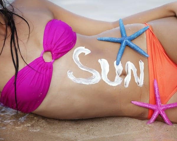 female sunbathing in bikini, the word "sun" is written with sun screen