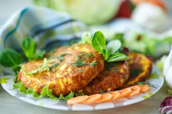 Three round kumara and halloumi fritters on a plate with decorative salad