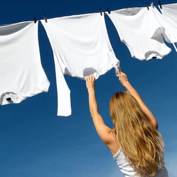 Longhaired young woman reaching white laundry which hangs to dry in a summer breeze on a clothes-line.
