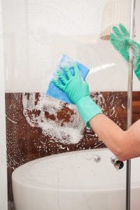 hands wearing blue gloves cleaning shower door