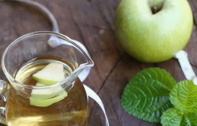 Pitcher of switchel with green apple and mint on a wooden table
