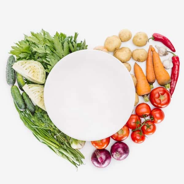 colourful vegetables in a heart around a white plate
