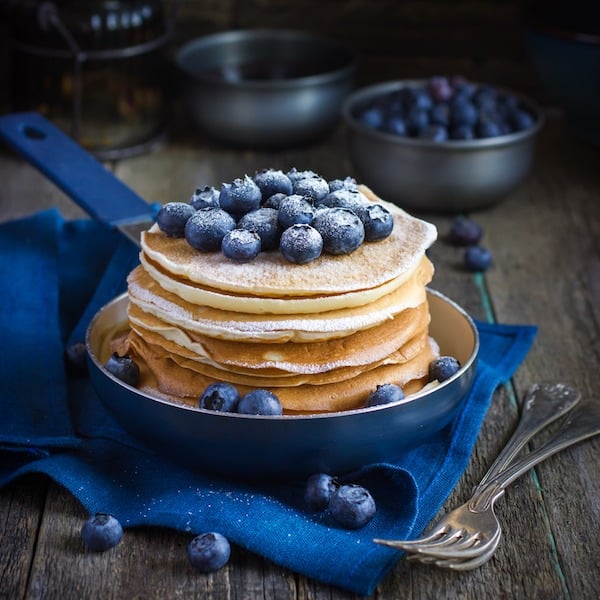 pancakes with blueberry and powdered sugar in pan on rustic background, square image