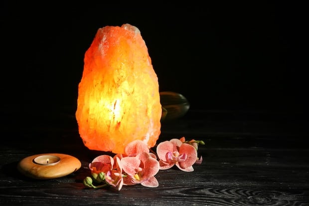 Himalayan salt lamp, candle and flowers on table against dark background