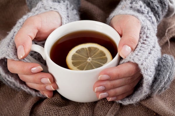 Woman's hand holding cup of tea with lemon on a cold day